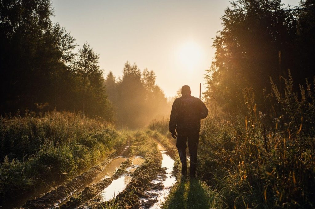 A man walking along a muddy path surrounded by trees in a dense forest