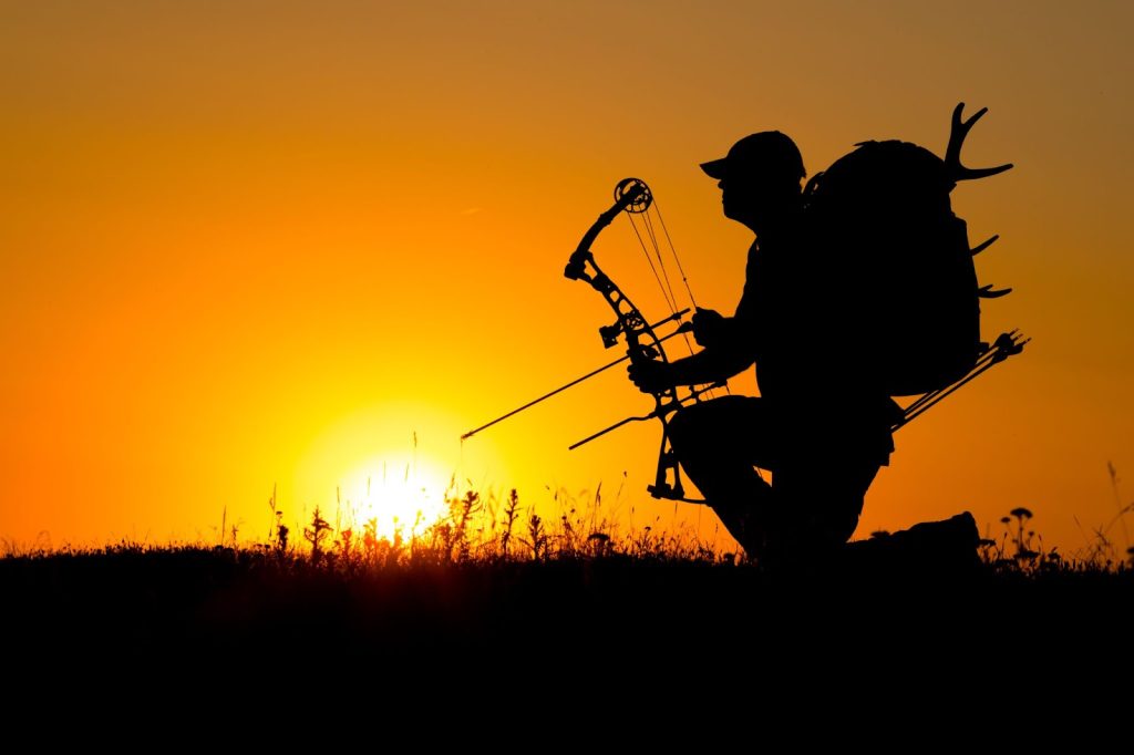 A silhouette of a man with a bow and arrow against a sunset sky