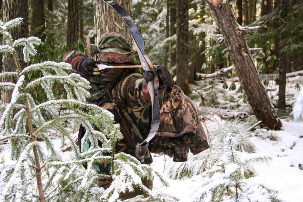 A hunter in camouflage gear takes aim at a tree during a guided hunt for elk, organized by a hunting company.