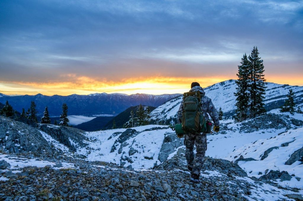 A man with a backpack hikes a mountain trail at sunset amidst colorful skies