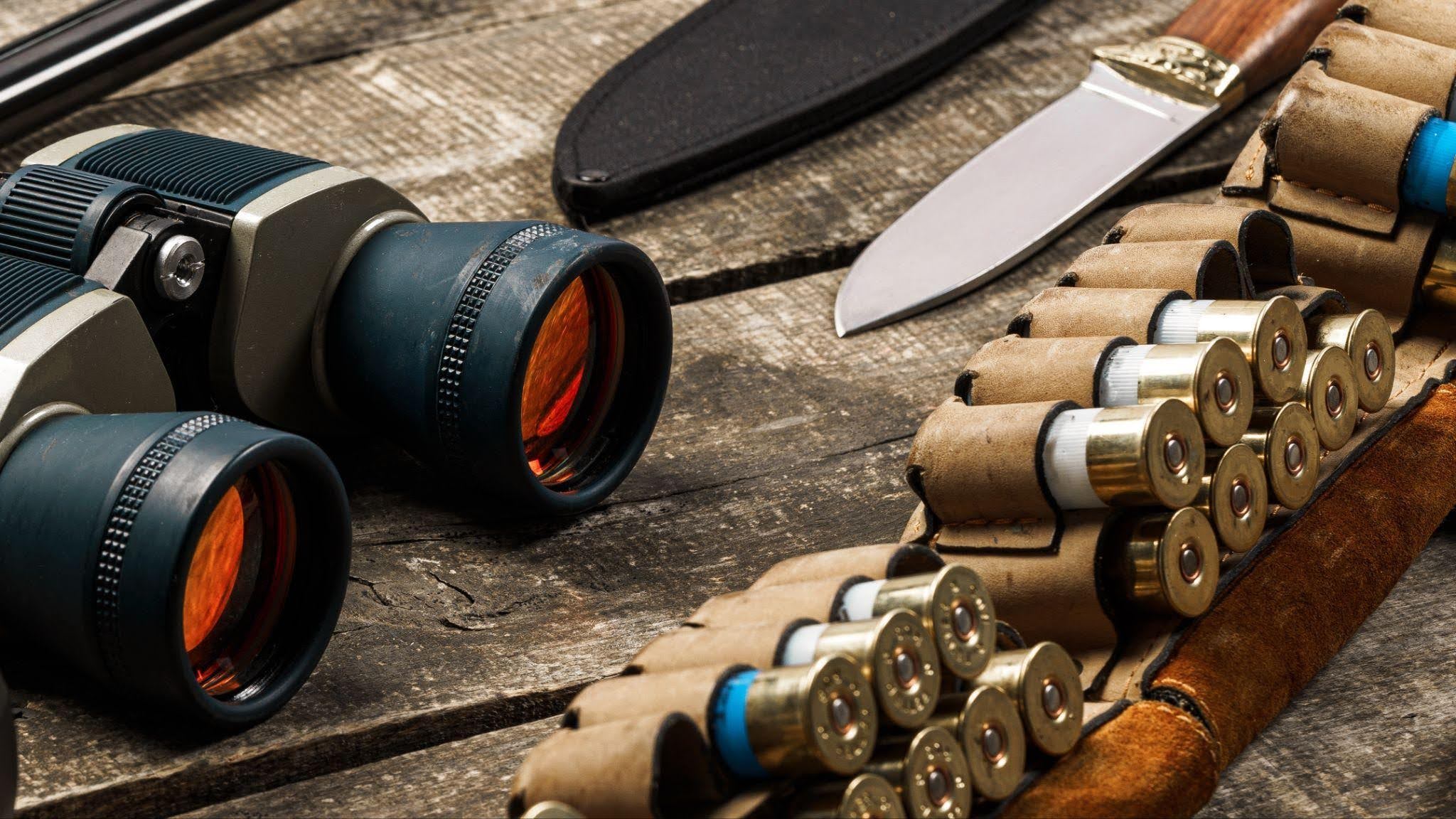 A wooden table features a pair of binoculars a knife and a gun highlighting outdoor or survival gear