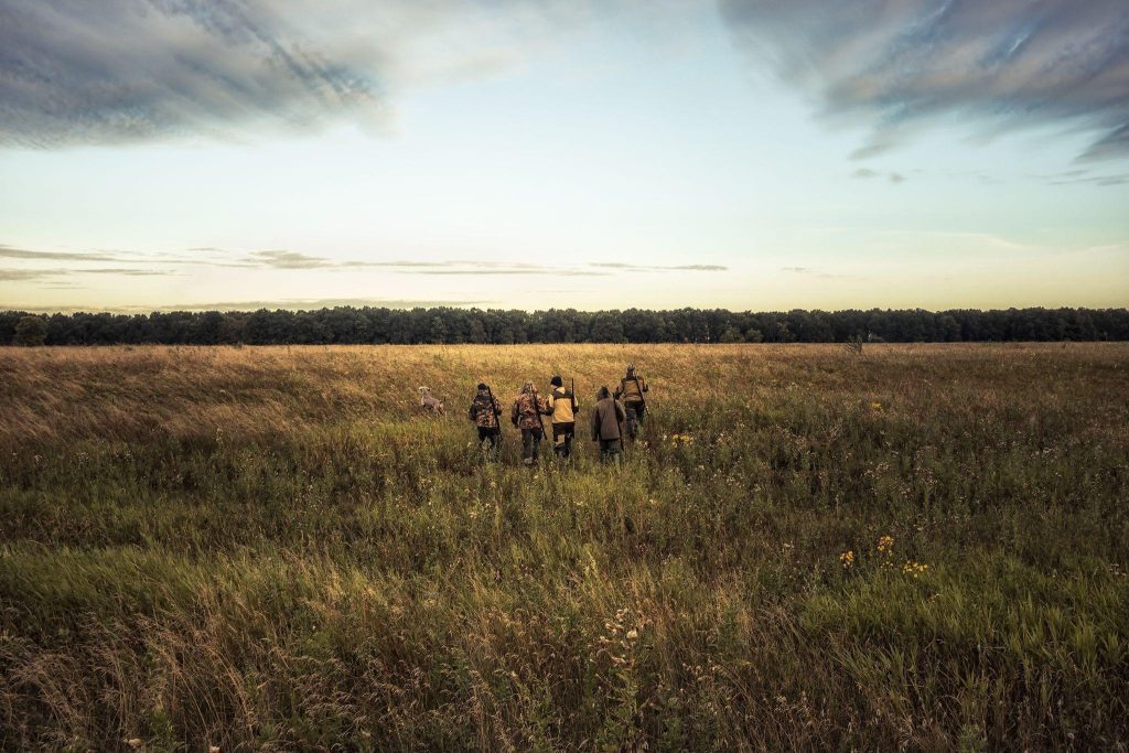 A diverse group of people standing together in a green field smiling and enjoying the outdoors